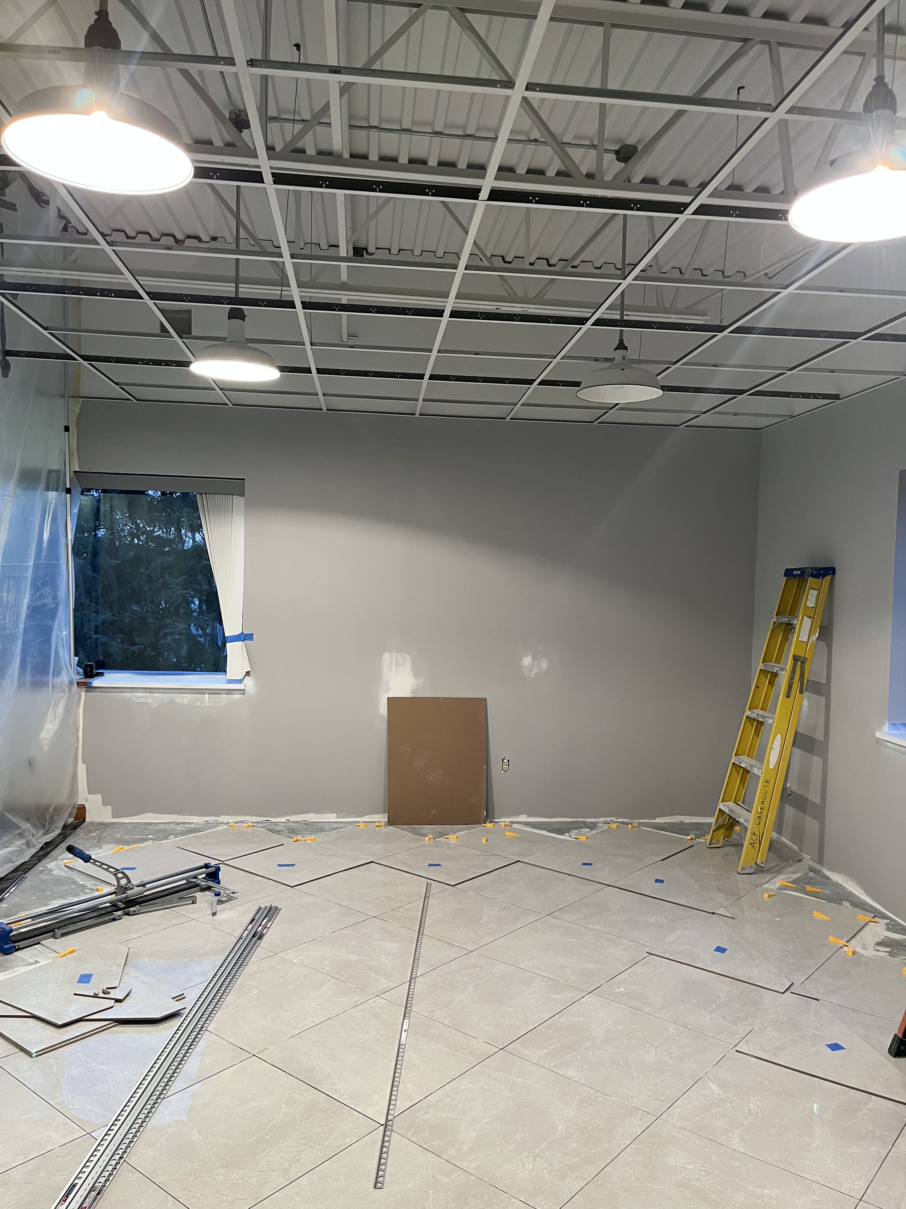 Commercial room with ceiling grid install and floor tile work in progress.