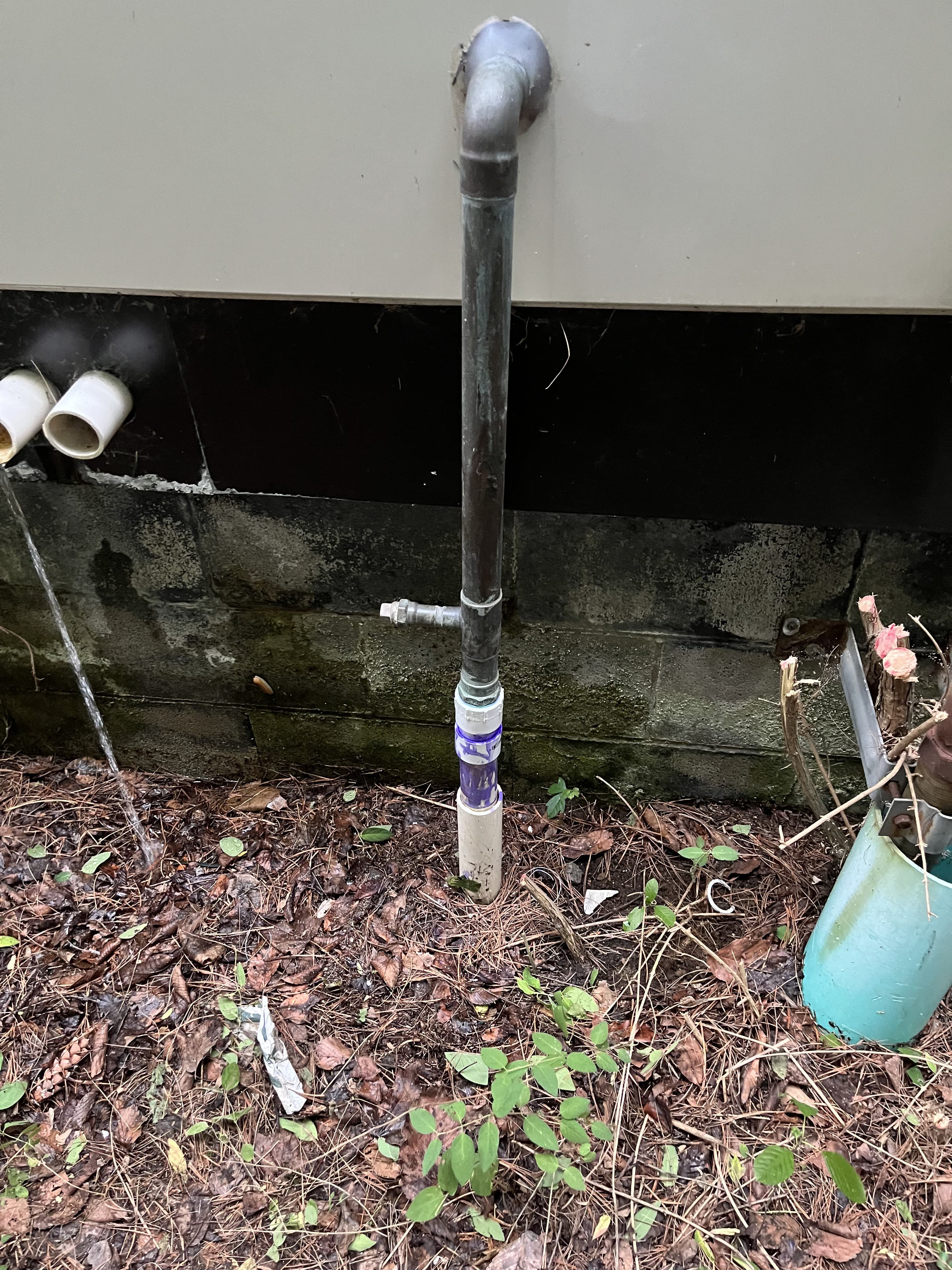 Exterior utility discharge repair detail beside a building wall.