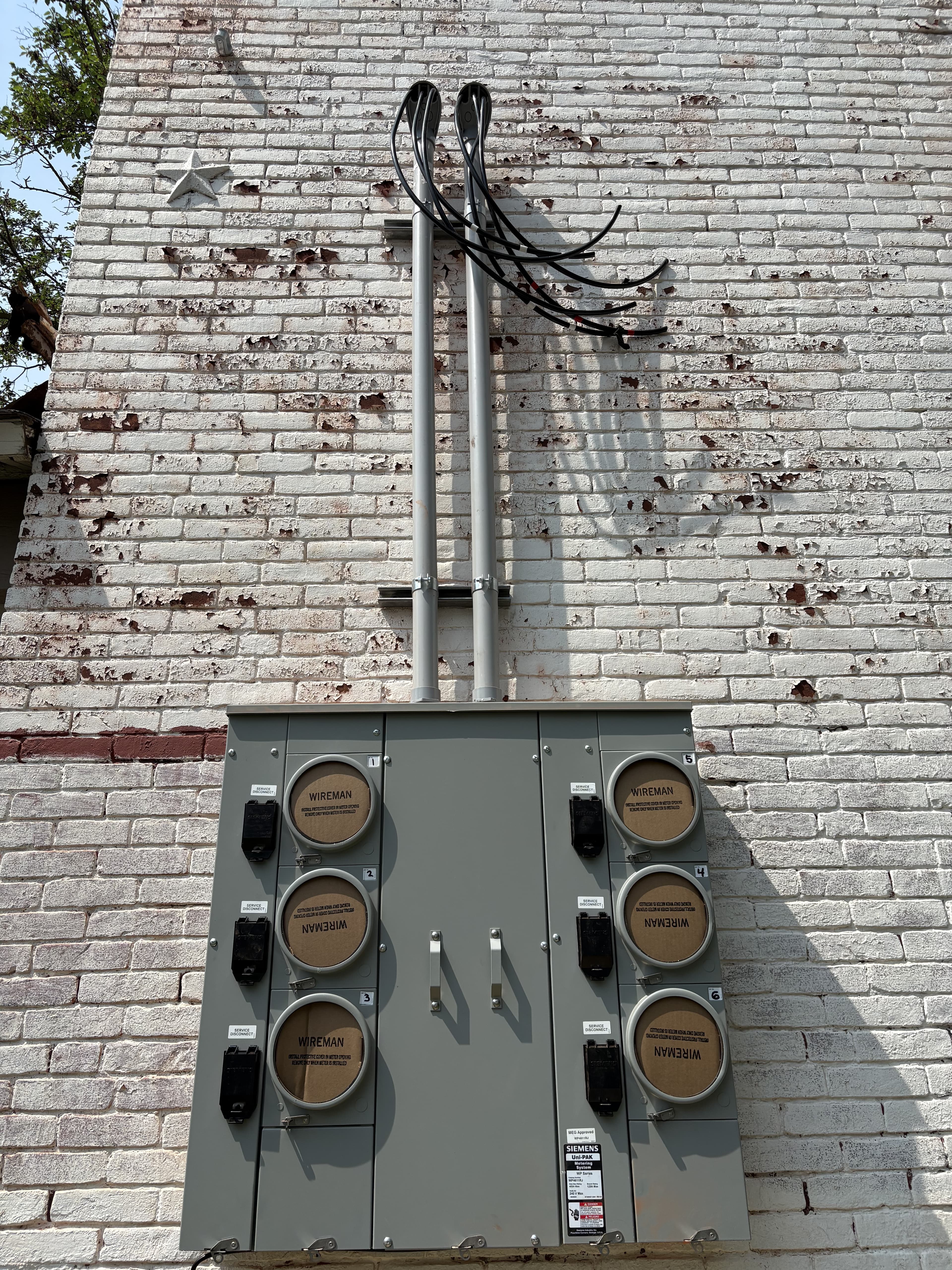 Multi-meter electrical service equipment mounted to an exterior brick wall.