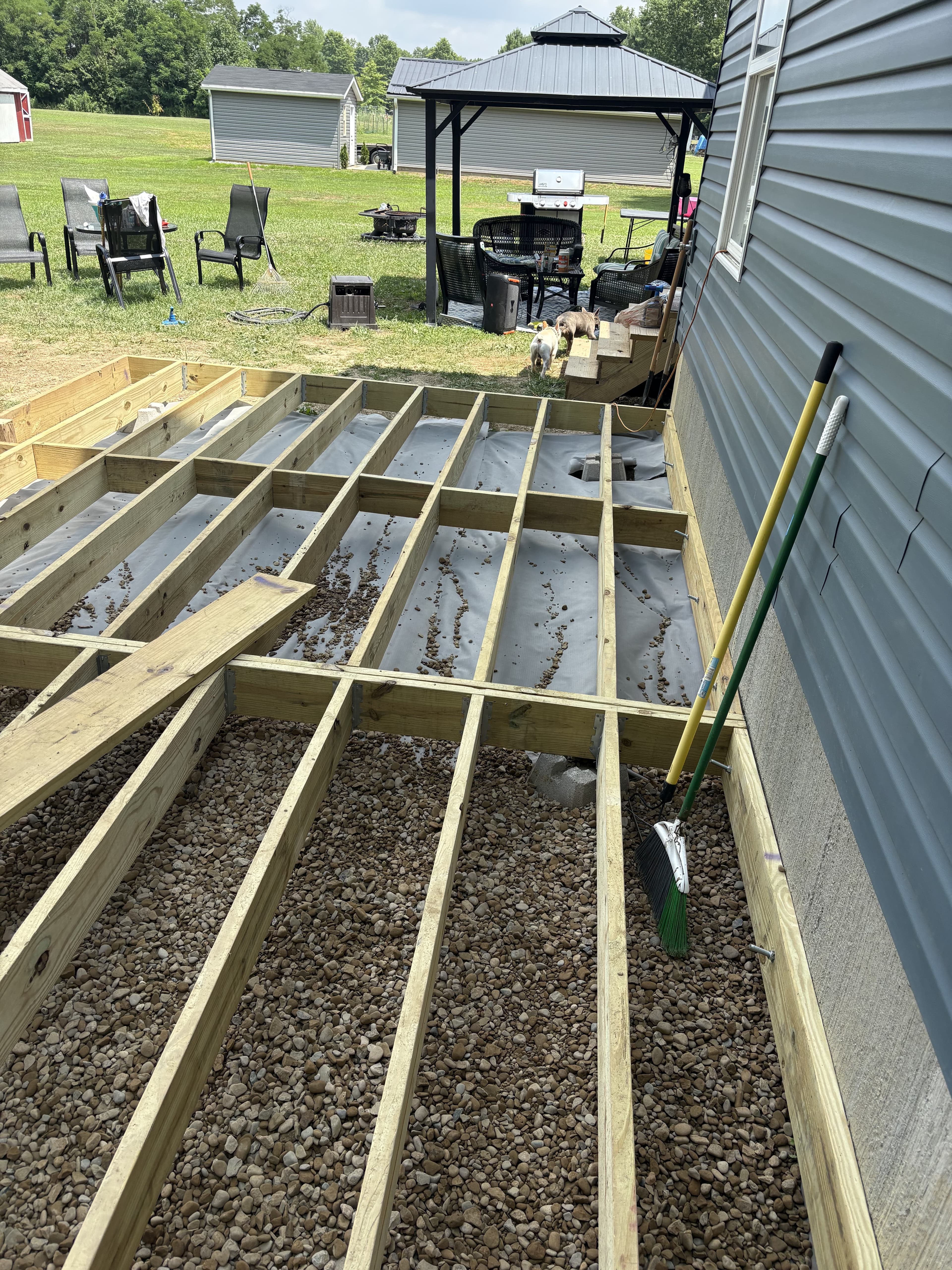 Deck framing and gravel base under construction beside a house.