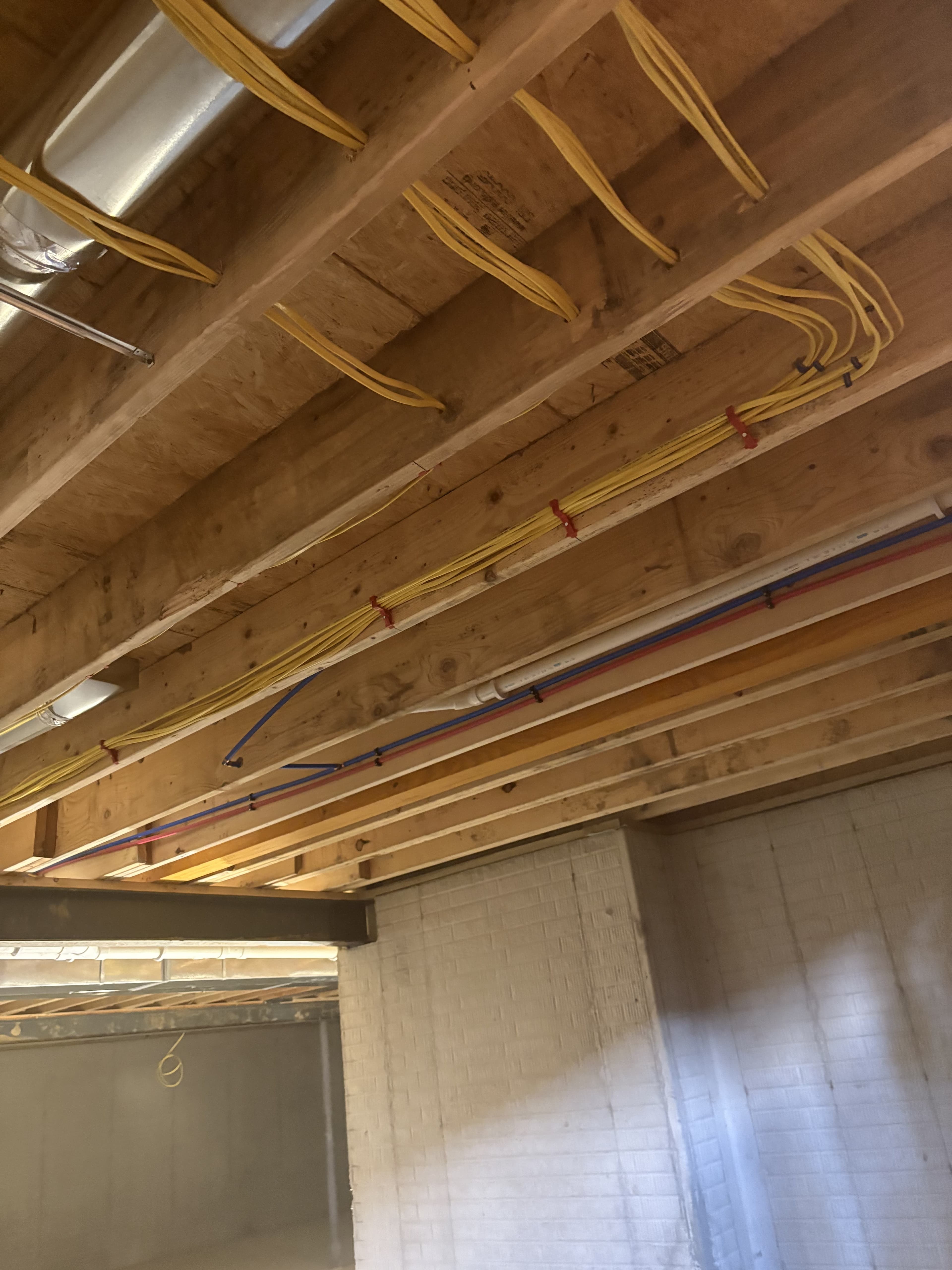 Electrical wiring laid out across joists in an unfinished ceiling.