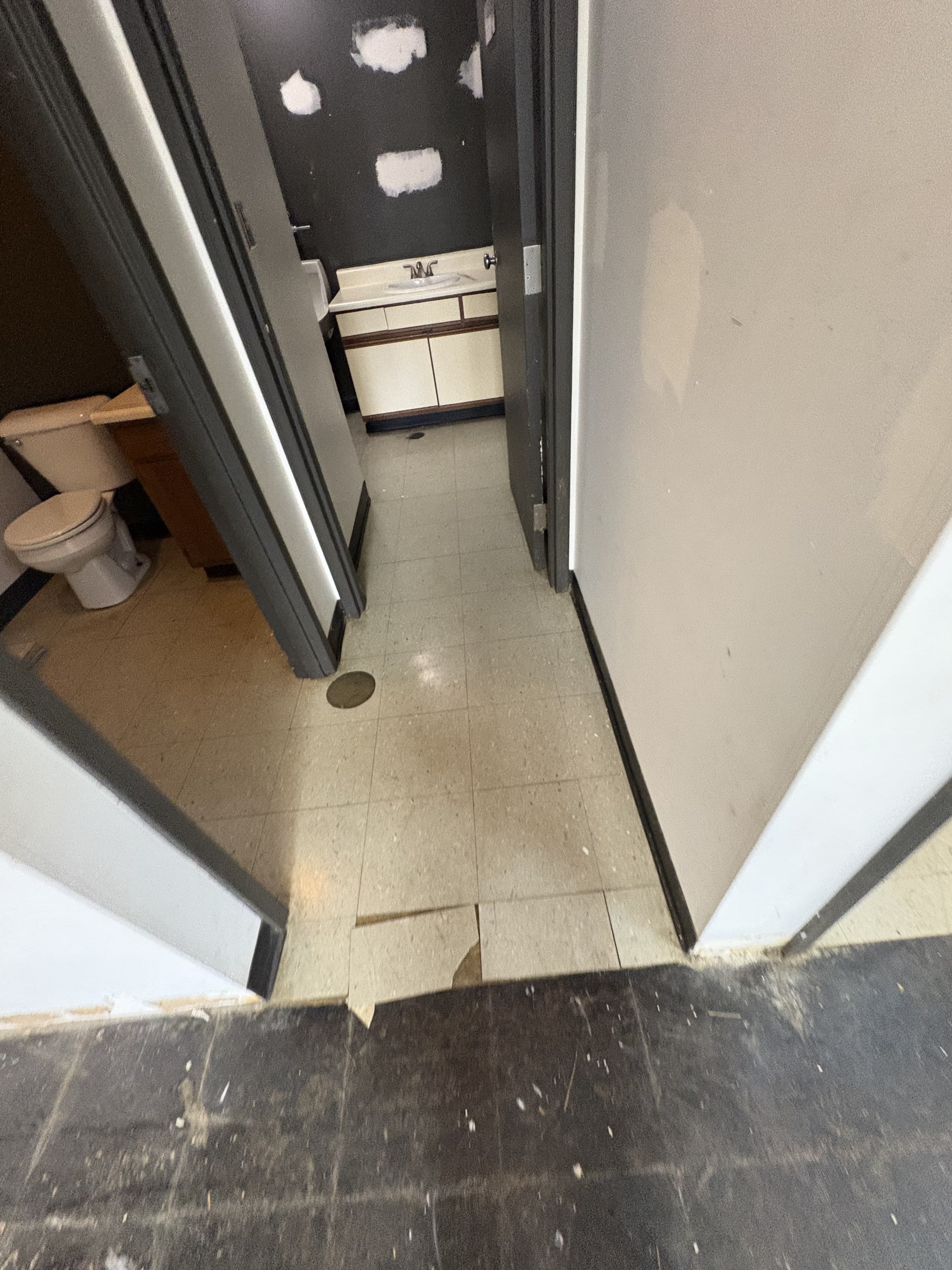 Commercial restroom entry with patched walls and exposed floor prep during remodeling.