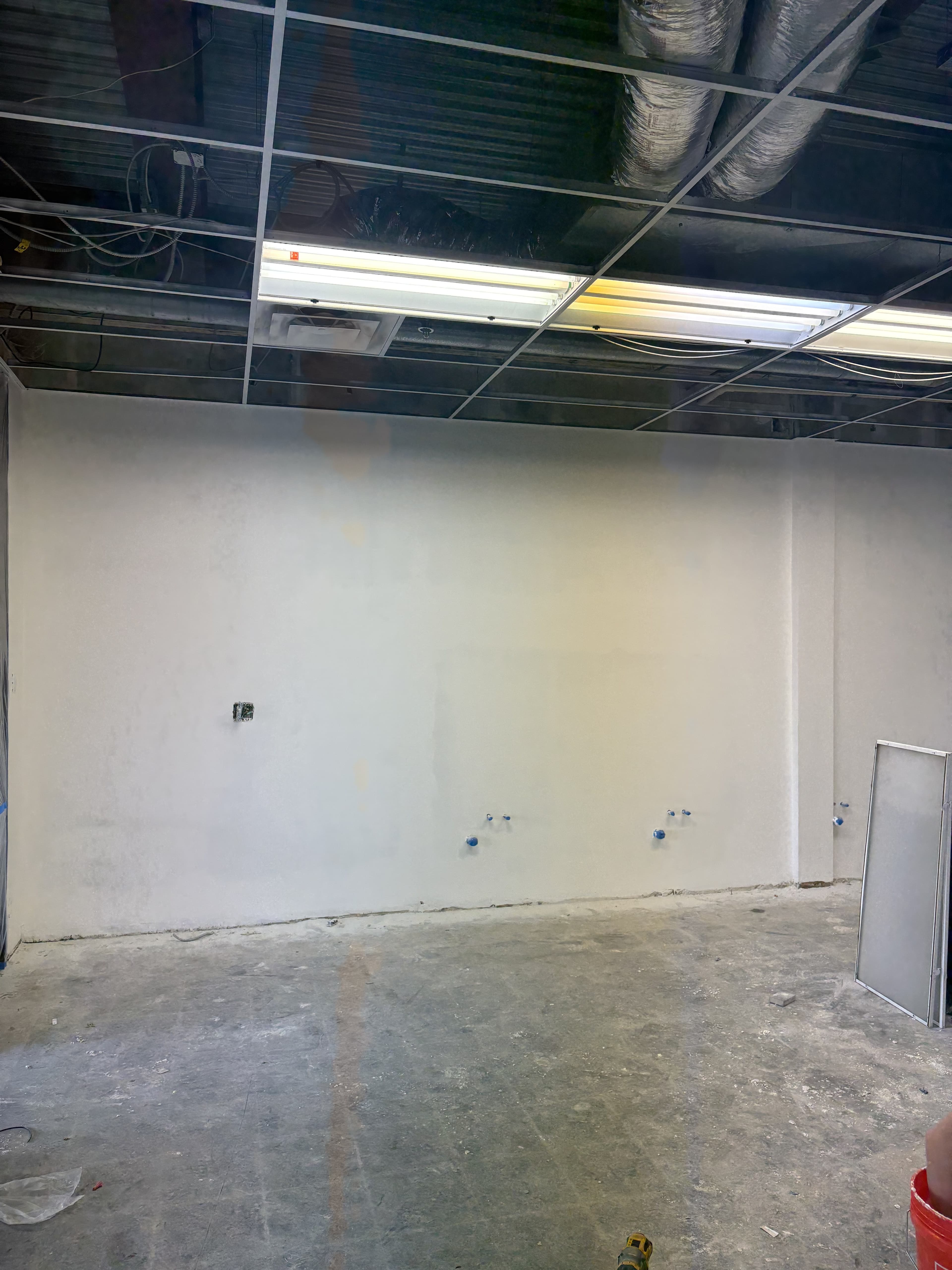 Commercial room with an open ceiling grid, patched walls, and floor prep during renovation.