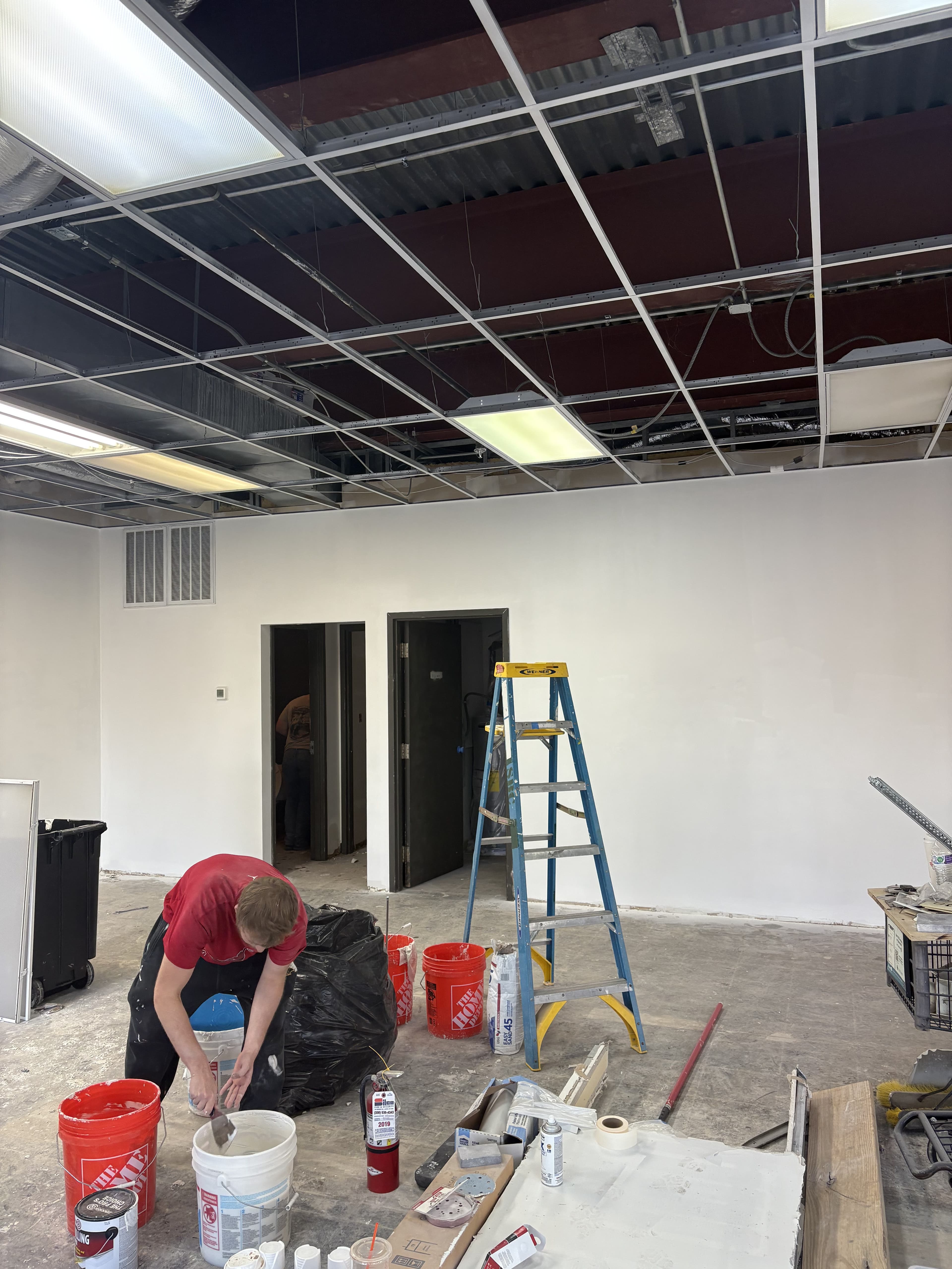 Commercial room during build-out with open ceiling work and jobsite access visible.