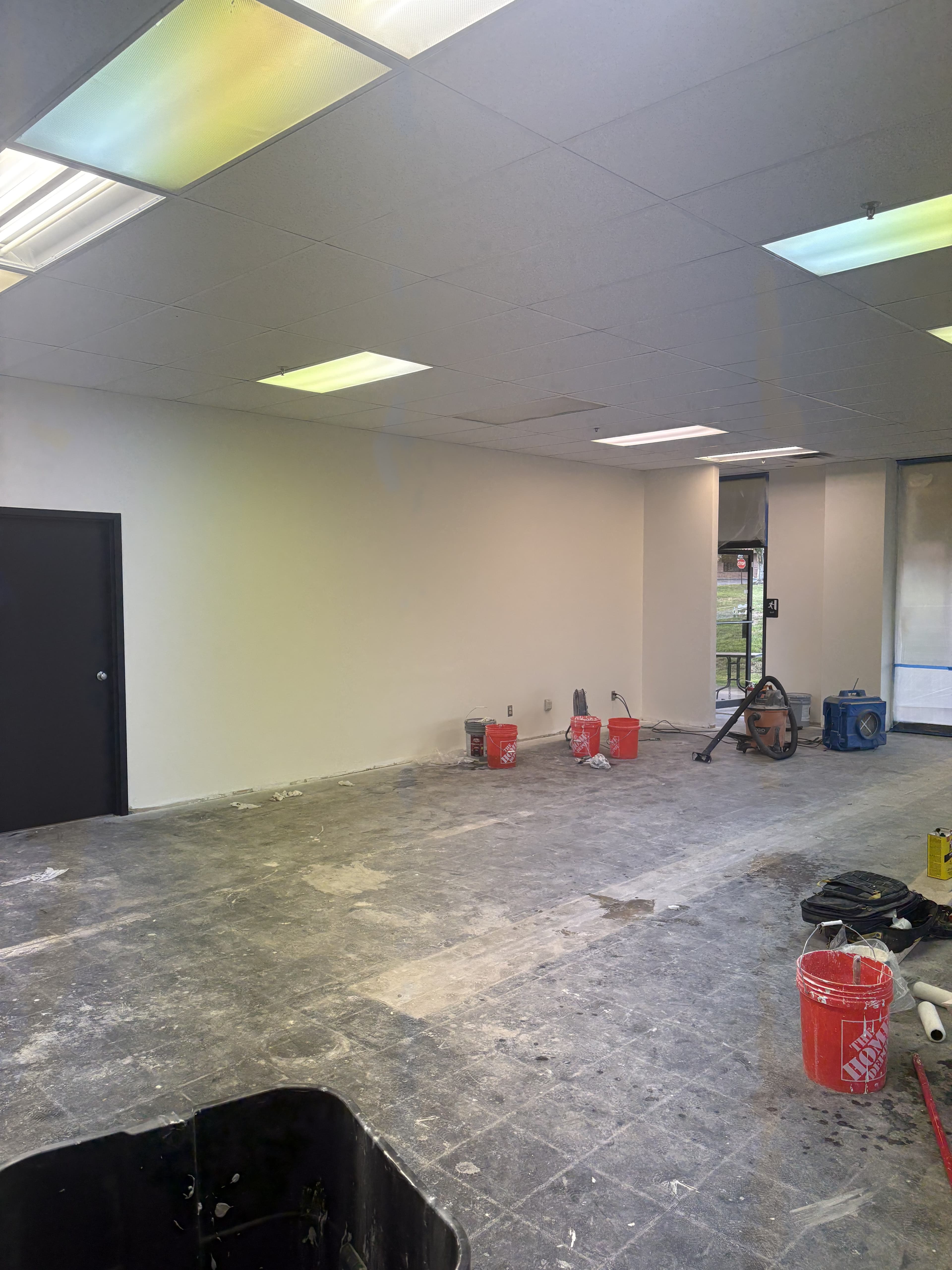 Commercial room with finished walls, installed ceiling tiles, and stripped floors awaiting final finish work.