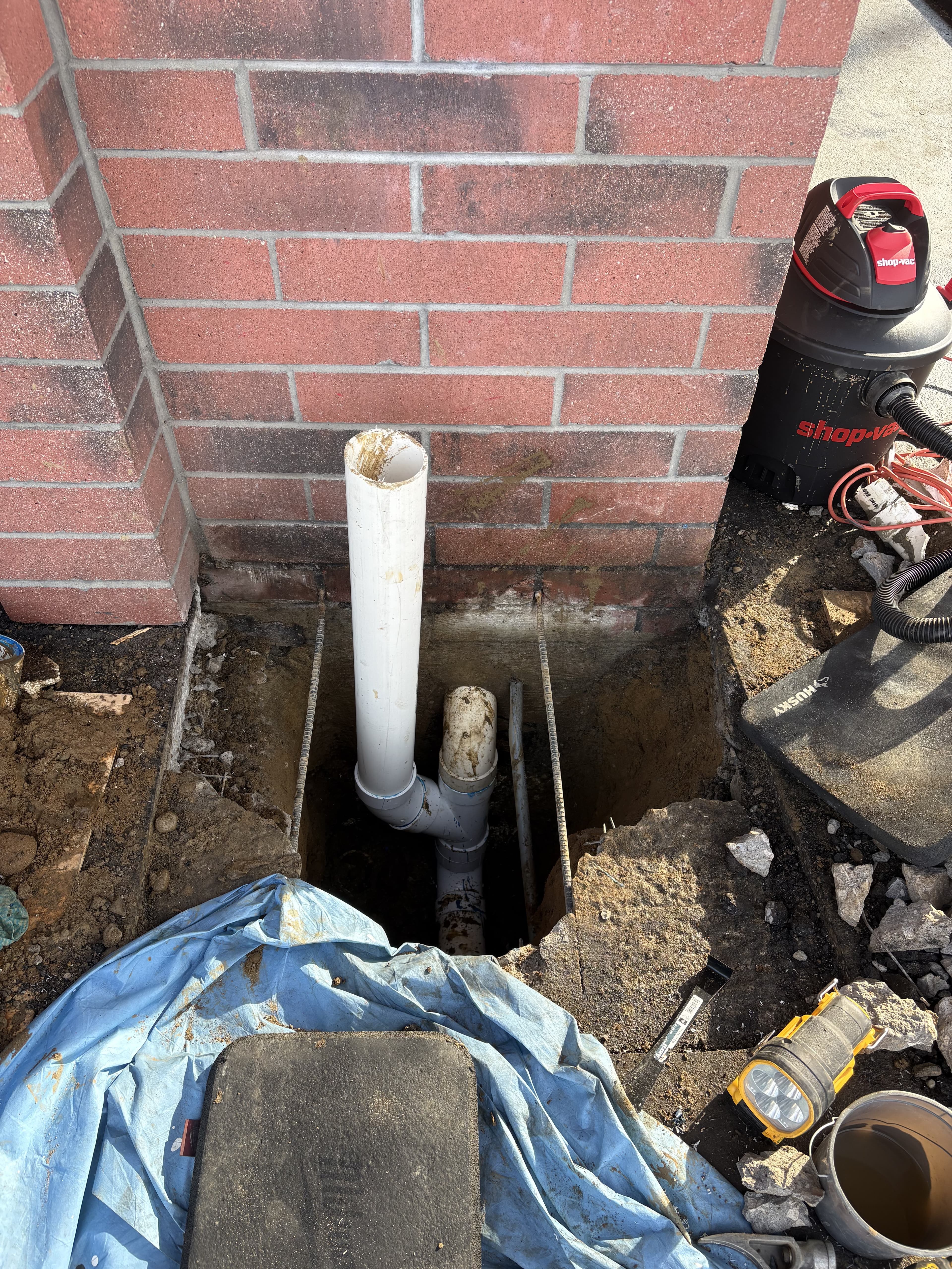 Drainage repair excavation beside a brick wall.