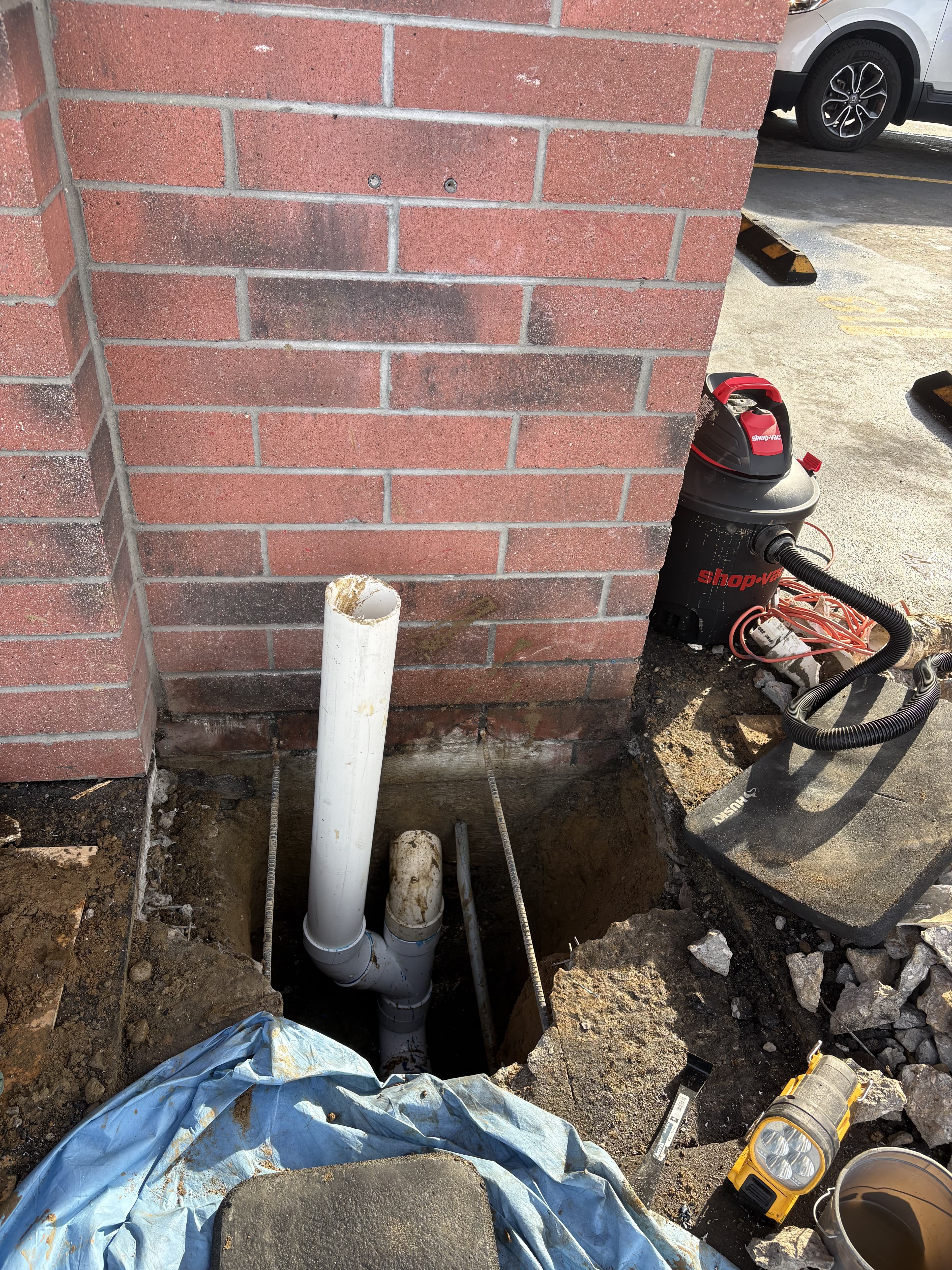 Close view of drainage repair excavation beside brick.