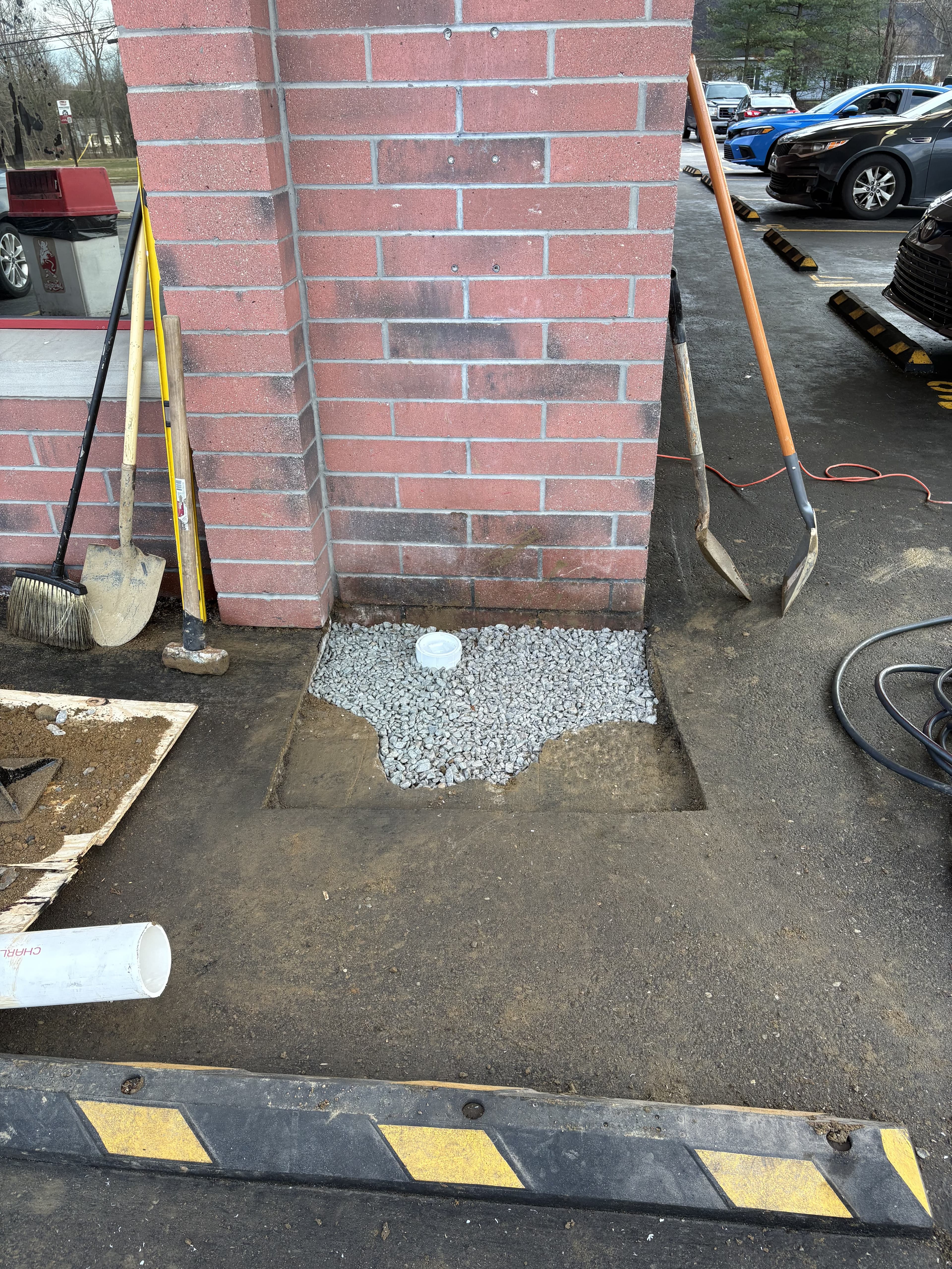 Drainage repair patch in progress beside brick wall.