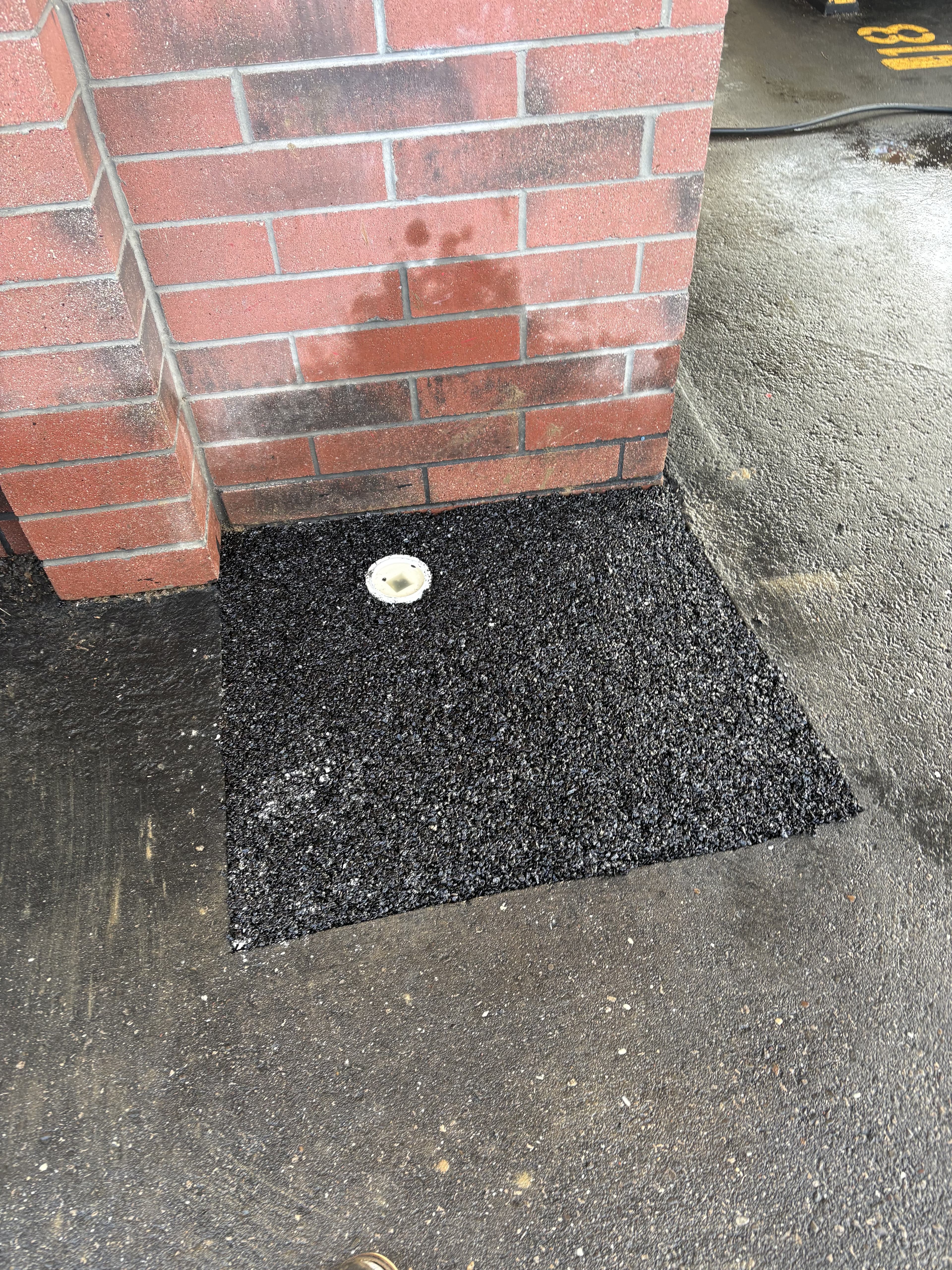 Completed drainage repair patch beside brick wall.